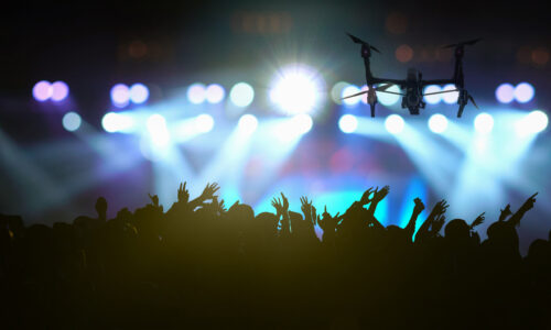 Closeup silhouette of Drone flying for taking video of Concert crowd in silhouettes of Music fanclub with show hand action which follow up the songer at the front of stage with follow light