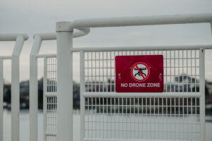 Sign with “NO DRONE ZONE” written on a red square metal attached to a fence